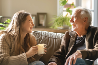 Senior und junge Frau sitzen auf dem Sofa, reden miteinander und trinken Tee